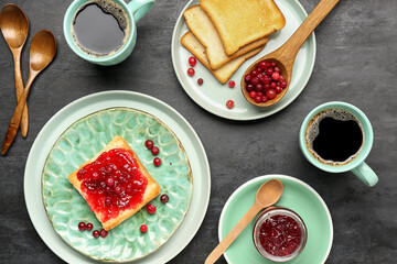 Tasty toasts with cranberry jam and cups of coffee on dark background