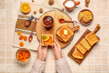 Woman eating tasty toasts with apricot jam on light tile background
