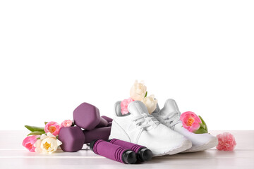Obraz na płótnie Canvas Sneakers with spring flowers and sports equipment on table against white background