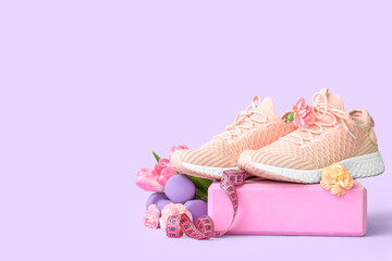 Sneakers with spring flowers, sports equipment and tape measure on lilac background