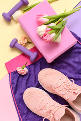 Sportswear with spring flowers and equipment on color background