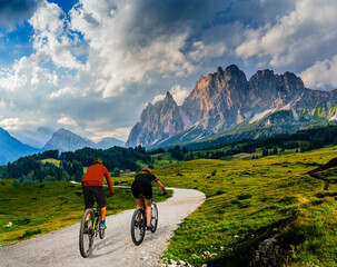 A man and woman ride electric mountain bikes in the Dolomites in Italy. Mountain biking adventure on beautiful mountain trails. - 589784267