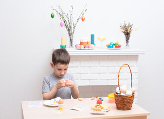 Child boy decorating and painting easter eggs against defocused fireplace with Easter decorations...