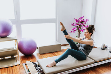 latin woman doing pilates exercises on reformer bed at home in Mexico, hispanic people