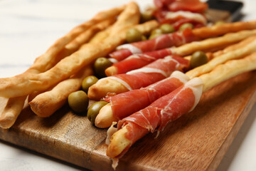 Wooden board of tasty Italian Grissini with bacon on table, closeup