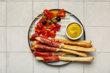 Plate of tasty Italian Grissini with bacon on white tile background
