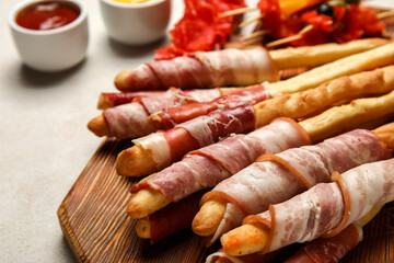 Wooden board of tasty Italian Grissini with bacon on light background, closeup