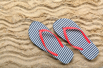 Striped flip-flops on sand, top view