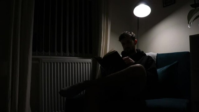 Silhouette shot of man sitting in a corner with a lamp reading his book