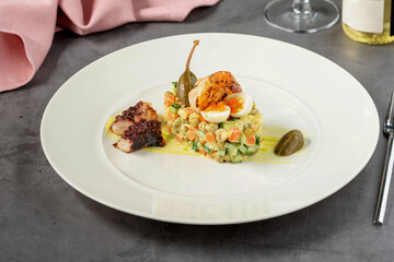 Russian salad with aioli sauce, shrimp, octopus and capers on a white porcelain plate