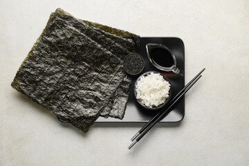 Nori sheets with rice, sesame seeds and sauce on light background