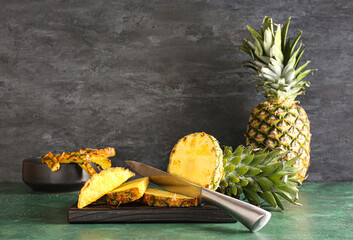 Wooden board with cut pineapple on color table near black wall