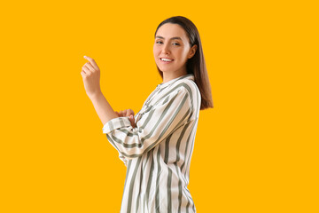 Beautiful young woman rolling up her sleeve on yellow background