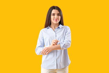 Beautiful young woman rolling up her sleeve on yellow background