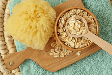 Oat flakes in wooden bowl with spoon and sponge on chopping board and towel - Natural beauty ingredients