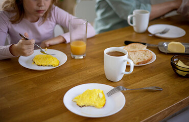 Side view of a family having breakfast in the kitchen with an omelette, a sandwich with butter and cheese, orange juice and coffee. Delicious and healthy breakfast. Selective focus on the coffee mug.