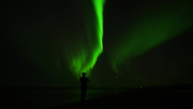 Silhouette showing man with smartphone taking picture of green Northern Lights at night sky