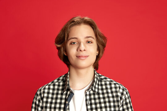 Close Up Portrait Of Young Boy Wearing Checkered Shirt Looking At Camera With Fake Smile Over Red Studio Background