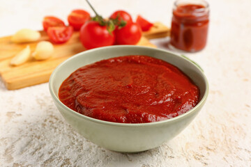 Bowl with tasty tomato paste on light background, closeup