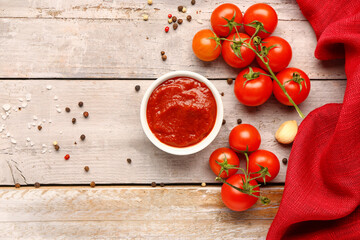 Bowl with tasty tomato paste and fresh vegetables on light wooden background