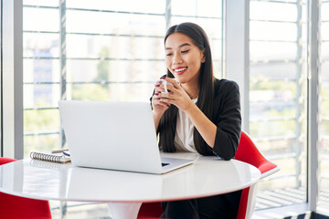 Happy Vietnamese student in modern university using laptop drinking coffee