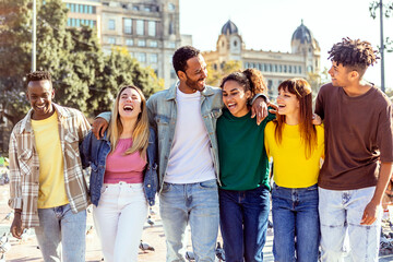 Group of six multiethnic happy friends hugging each other walking in city street. United group of millennial people enjoying day off together. Multiracial friendship and community concept