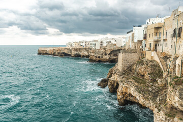 Fototapeta na wymiar Polignano a Mare, Bari, Italy. Old town built on the rocky cliffs. Traveling concept background with old traditional houses, dramatic cloudy sky and beautiful view of Mediterranean Sea