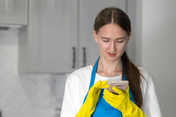 Beautiful caucasian woman in uniform uses a smartphone when cleaning the kitchen. Chat maid on a mobile phone. The au pair is looking for clients through the app. Smart Home