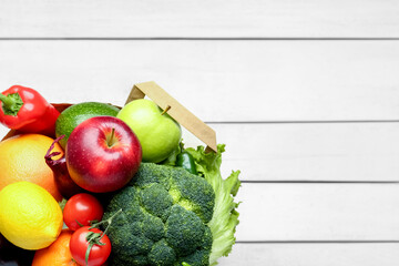 Paper bag with vegetables and fruits on white wooden background