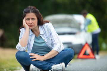 helpless woman sitting near broken red car