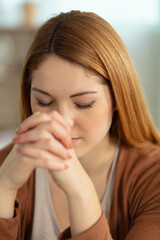 young woman at home with her eyes closed in prayer