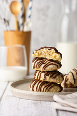 Nut cookies with chocolate icing. A stack of crispy biscuits on a plate, with pastry utensils, a glass and a bottle of milk in the background.