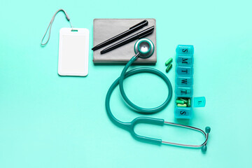 Stethoscope, notebook, badge and pills on turquoise background