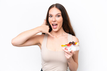 Young caucasian woman holding a bowl of fruit isolated on white background making phone gesture. Call me back sign