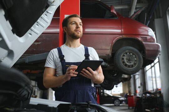 car mechanic using digital tablet with service and maintenance app on screen while inspecting vehicle in auto repair shop