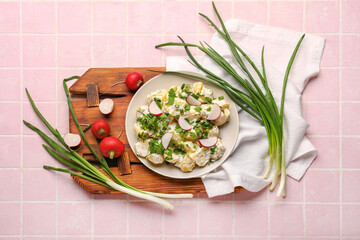 Plate of tasty Potato Salad with greens and radish on pink tile background