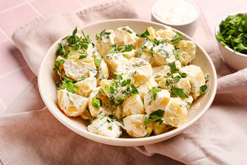 Bowl of tasty Potato Salad with greens on pink tile background