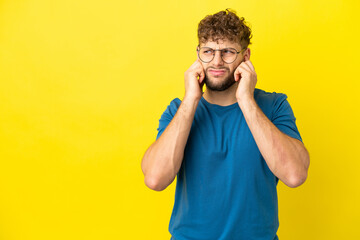 Young handsome caucasian man isolated on yellow background frustrated and covering ears