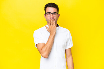 Young handsome man over isolated yellow background covering mouth with hand