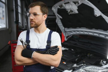 With tool in hand. Adult man in colored uniform works in the automobile salon