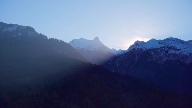 panning shot of light rays from rising sun coming from behind himalays onto the valley town of kullu manali showing this popular tourist destination during hot summers