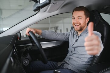 Successful and happy. Shot of a happy mature man smiling to the camera sitting in his brand new car at the local dealership