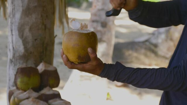 Man chopped the top off a green coconut with a machete. Street Vendor Cutting Coconut At the Tropical Beach. Natural fresh coconut juice. Close up hand of man choping fresh coconut shell.