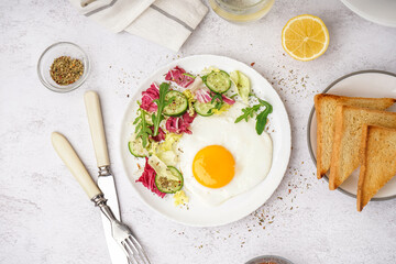 Plate with tasty fried egg, toast and salad on light table
