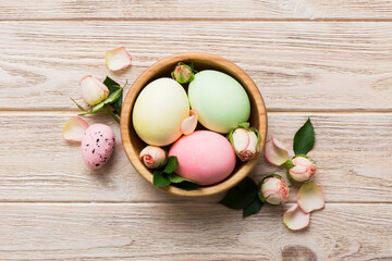 Happy Easter. Easter eggs in basket on colored table with yellow roses. Natural dyed colorful eggs background top view with copy space