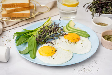 Plate with tasty fried eggs and greens on light table