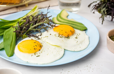 Plate with tasty fried eggs and greens on light table