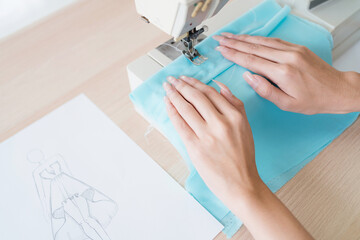 Close up hand of tailor woman sewing clothes with a sewing machine. A young attractive female fashion designer smile and look at the camera with clothes rack in the background in studio.