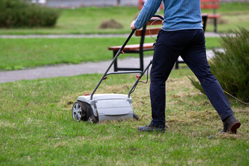 The gardener cuts the grass with a hand-held electric lawn mower.	