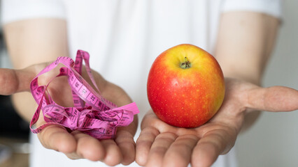 A man in his hands holds a glass of water and a red apple with a measuring tape. The concept of proper nutrition and a healthy lifestyle